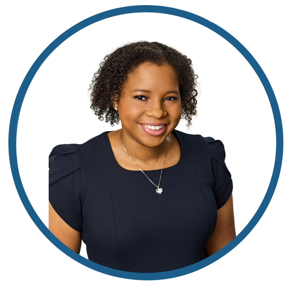 Smiling woman with curly hair in a navy dress and silver necklace.