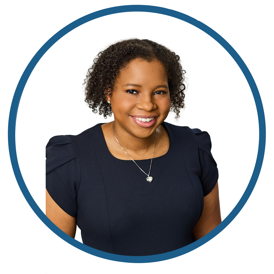Smiling woman with curly hair in a navy dress and silver necklace.